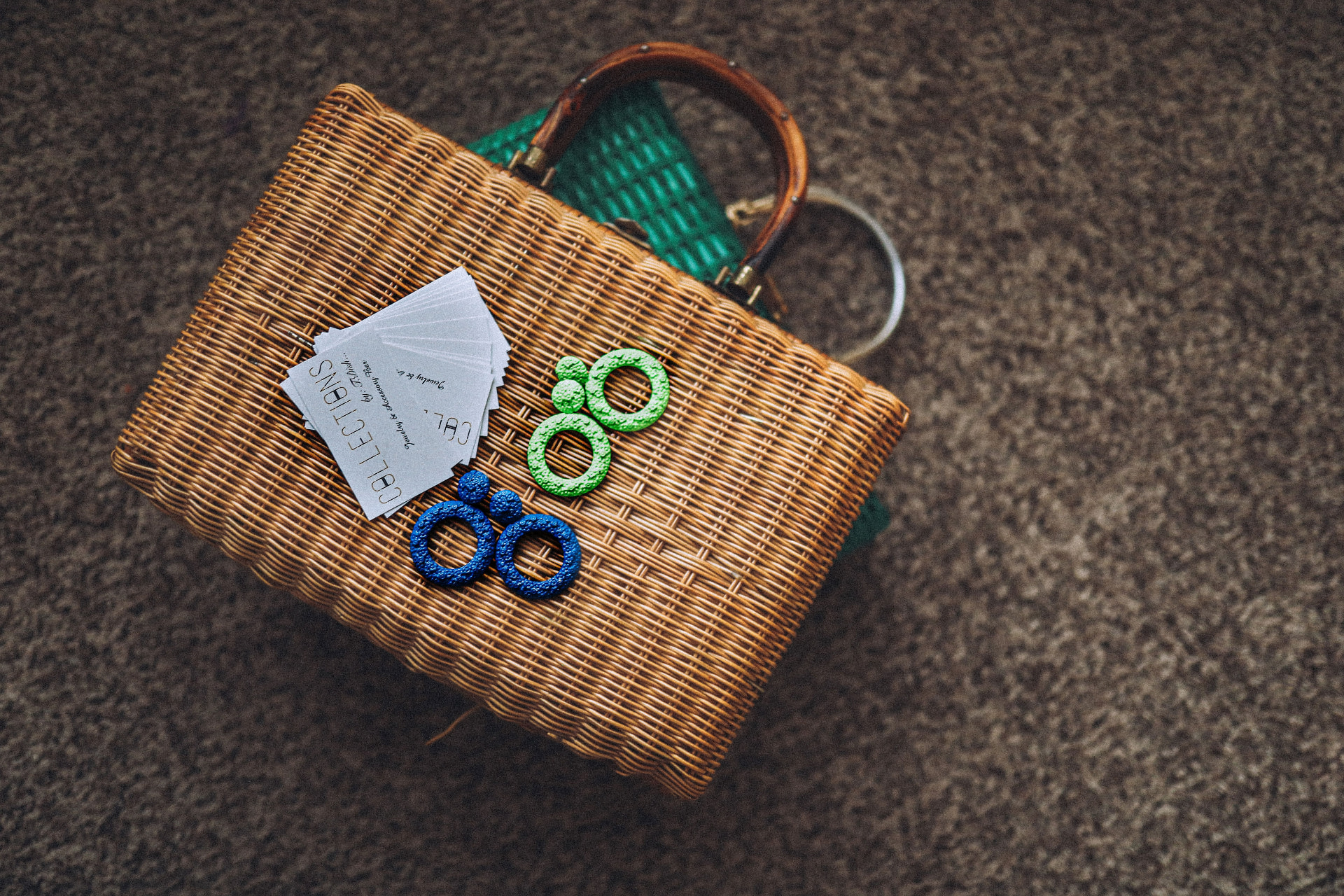 Wicker handbag styled with green and blue statement earrings and Collections business cards