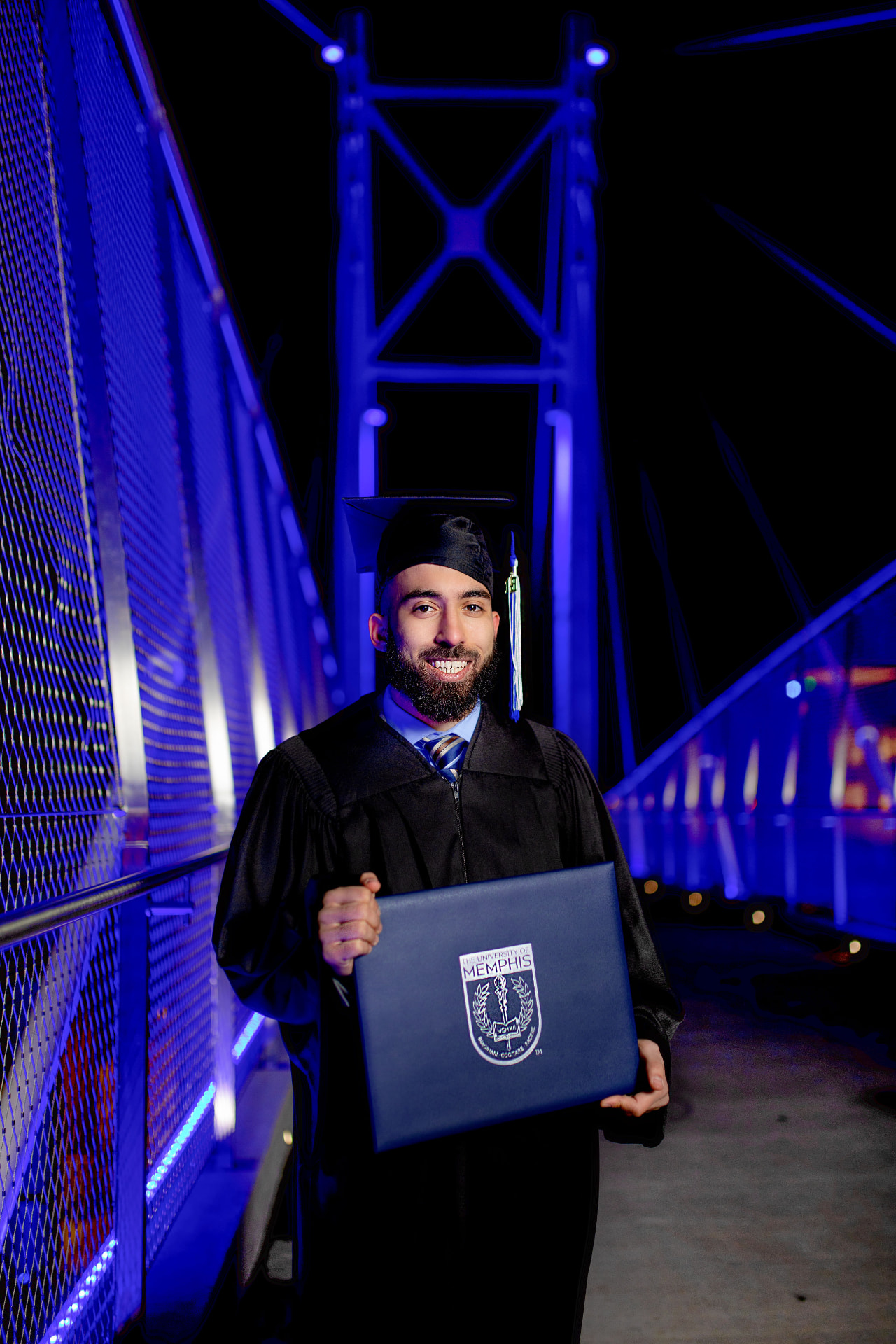 Graduate in cap and gown on a blue-lit bridge