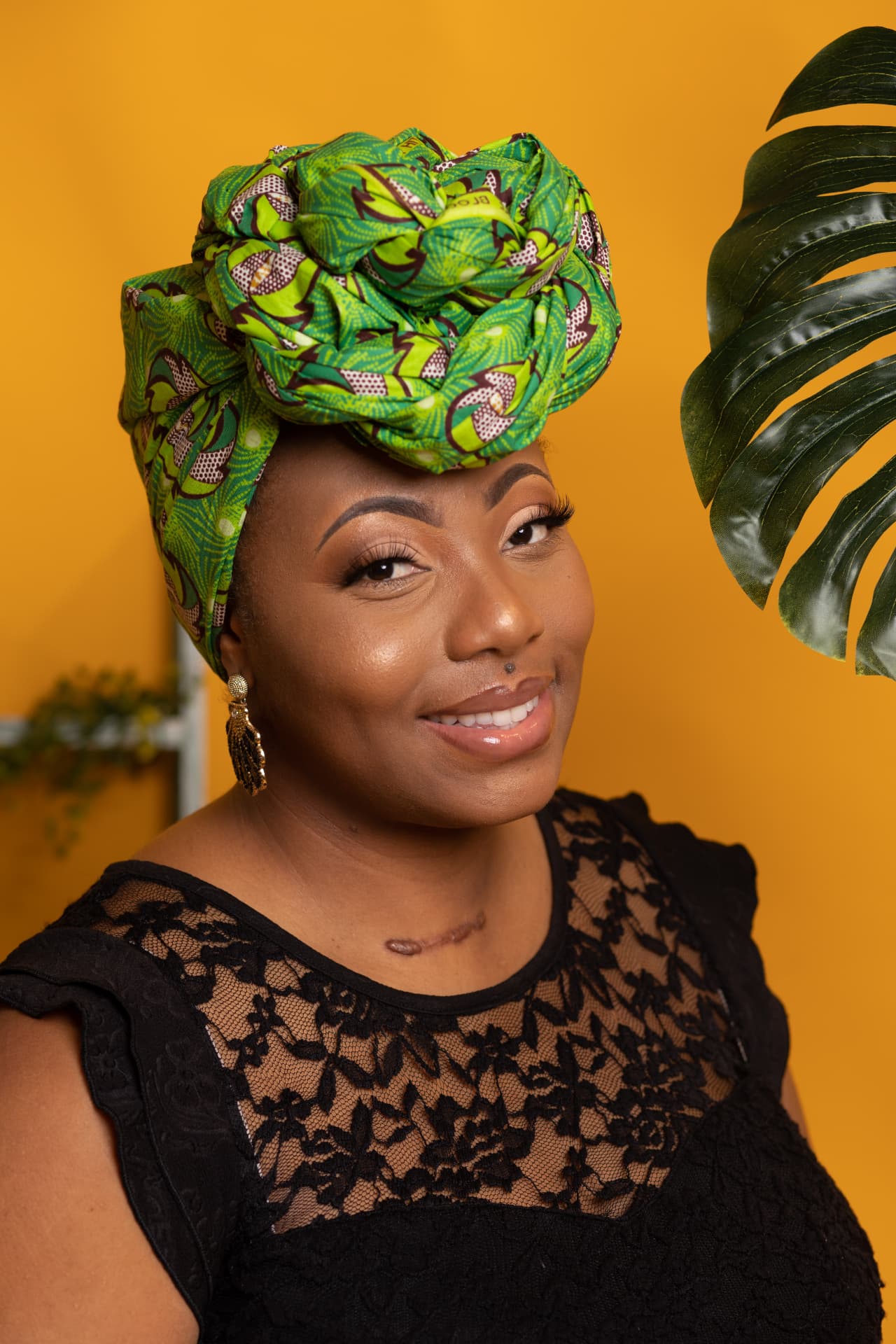 Personal brand portrait of a woman in a green head wrap against a golden yellow backdrop