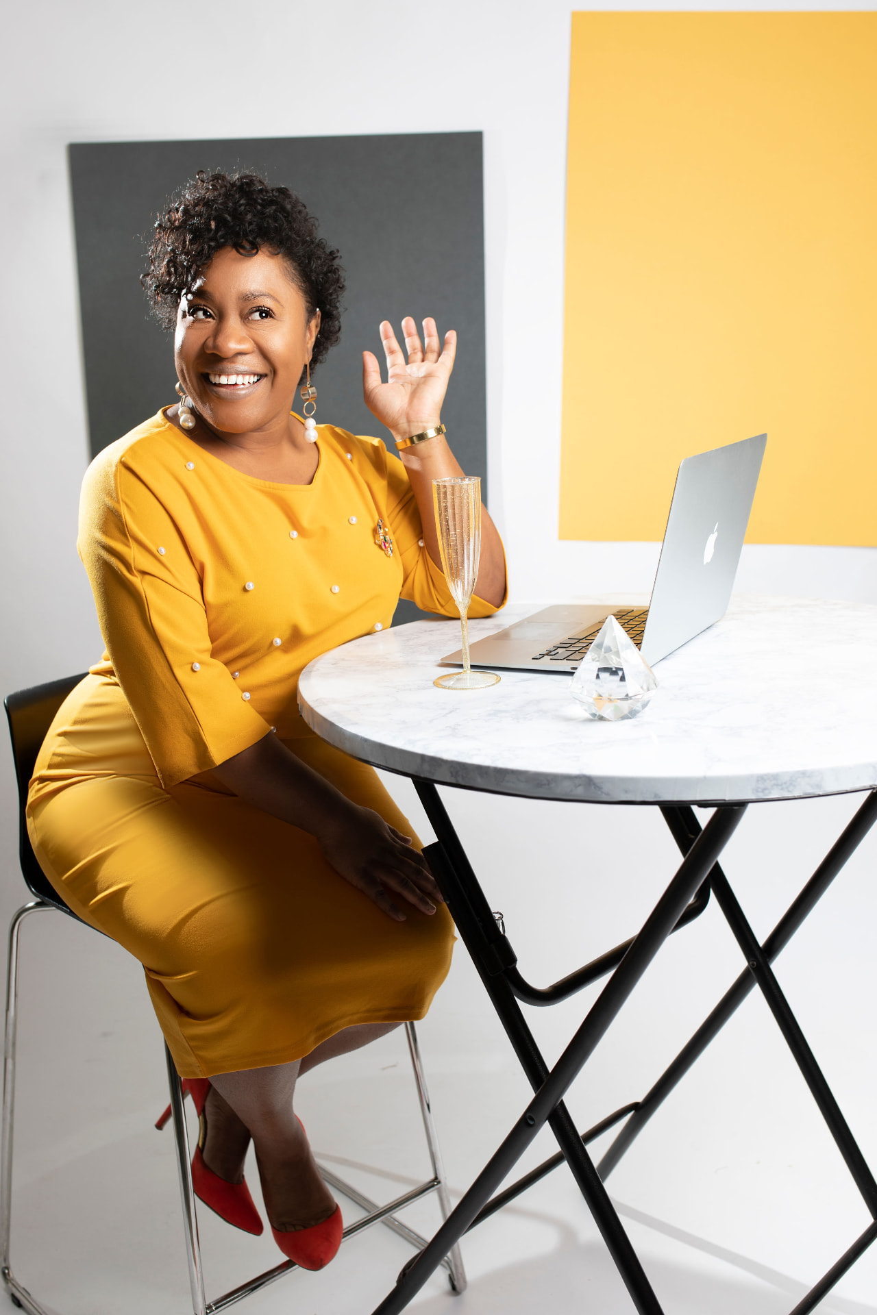 Entrepreneur in a yellow dress celebrating at a marble table with her laptop